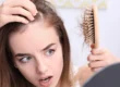 Worried young woman examining hair loss while holding a hairbrush with fallen hair and looking at thinning hairline in the mirror before Hair Restoration in San Antonio.