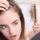 Worried young woman examining hair loss while holding a hairbrush with fallen hair and looking at thinning hairline in the mirror before Hair Restoration in San Antonio.